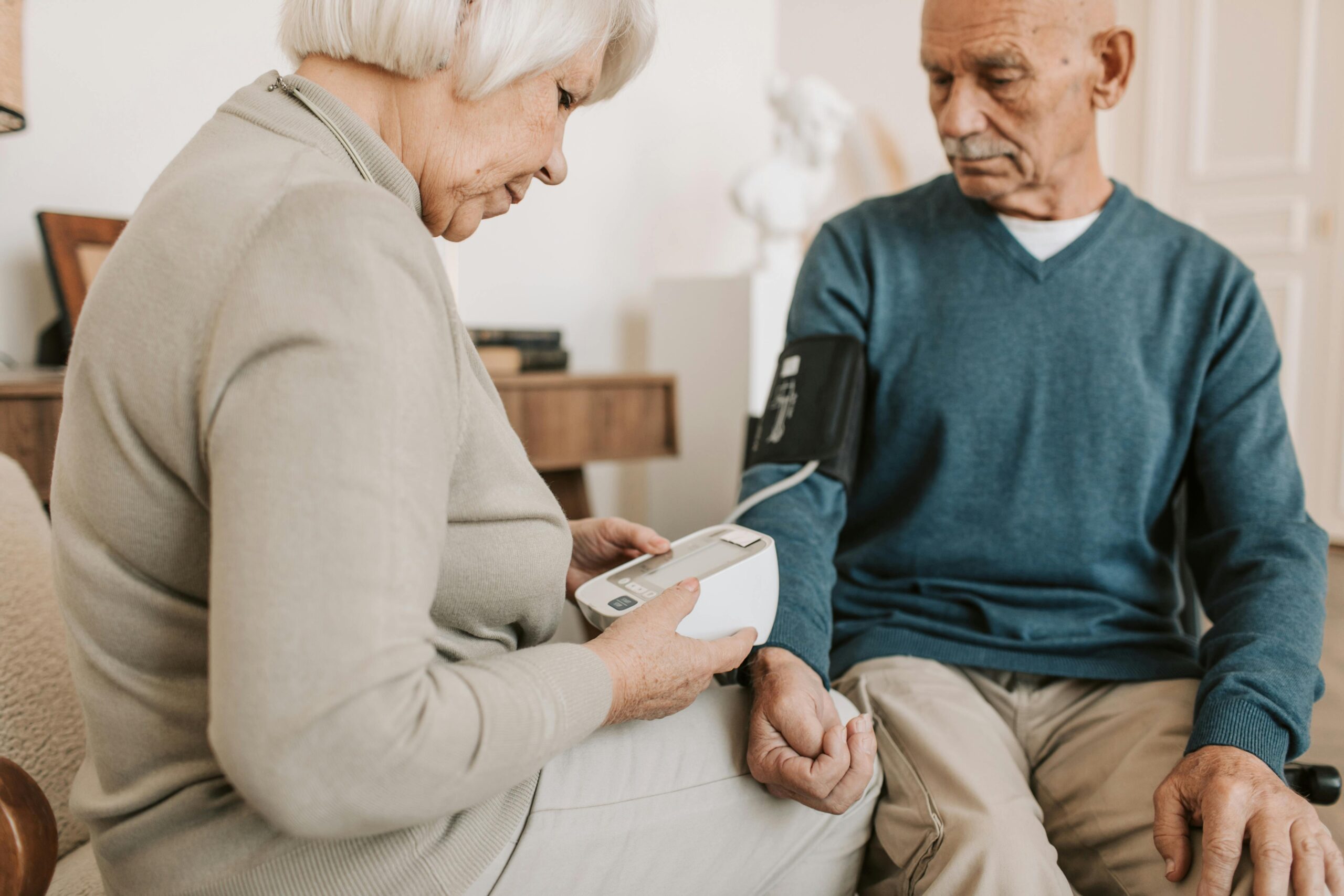 Senior couple at home using a sphygmomanometer to monitor blood pressure, promoting elderly health care.