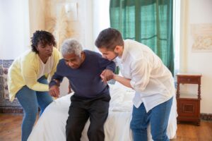 An elderly man receiving assistance from caregivers in a cozy home environment.